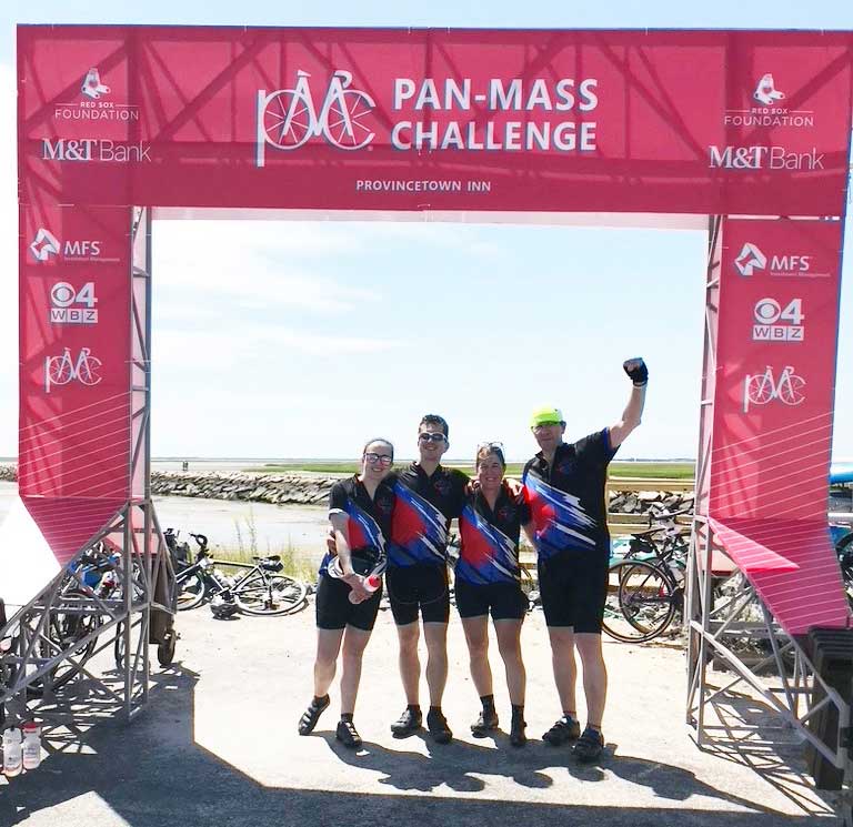 Four exuberant runners under an arch reading "Pan-Mass Challenge."