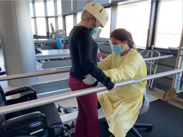 Jenn doing physical therapy on the walking bars, assisted by Rebecca Phelan.
