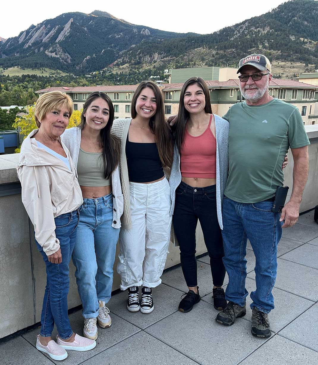 Kate with her parents and two sisters on a balcony, with the mountains behind them.