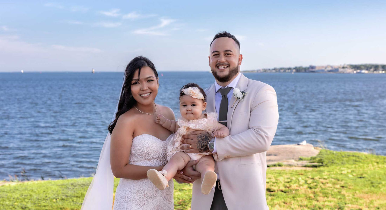 Katherine and her new husband Shawn in their wedding clothes, holding their baby, Amari, between them.