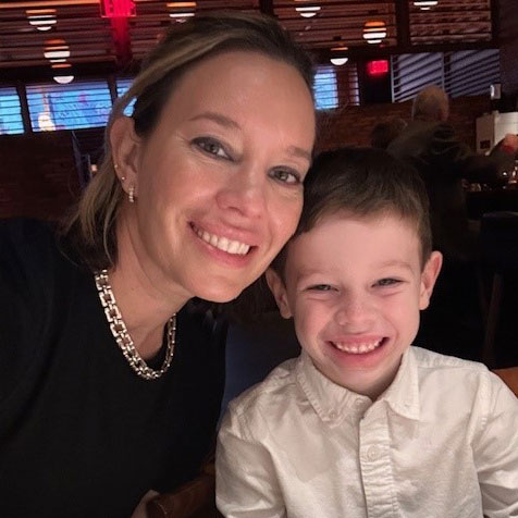 A woman and her 6-year-old son smile together in a restaurant.