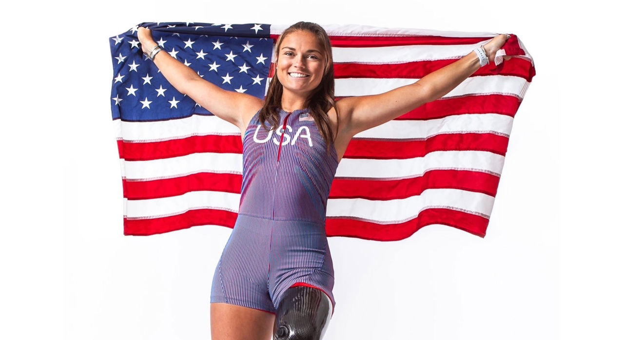 Noelle Lambert, U.S. paralympic athlete, holds an American flag behind her with part of her prosthetic leg visible.