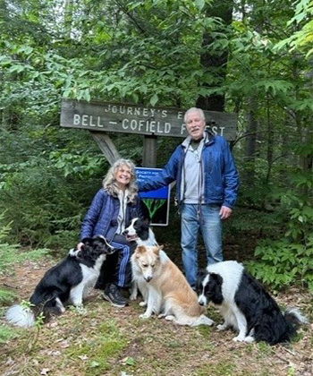 An older man and woman couple with their 4 dogs in the woods