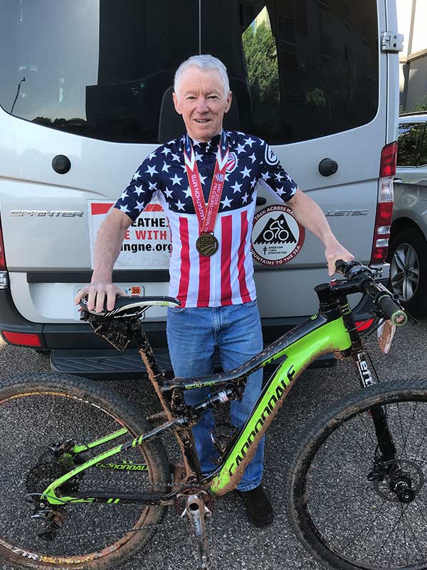 A competitive cyclist wearing a medal and standing with a bicycle