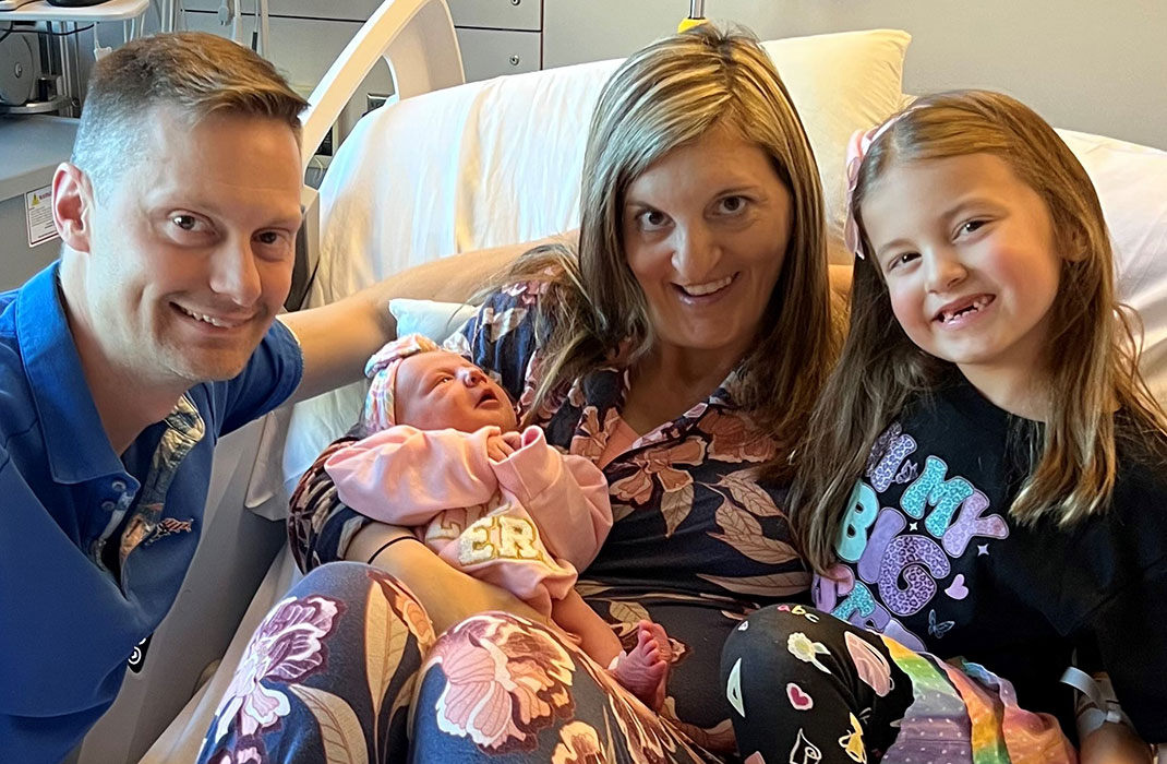 Stefania holds her newborn in the hospital, with her husband and older daughter at her side.
