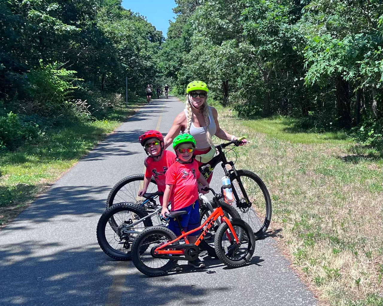 Tara and her two sons go for a bike ride on a sunny day in a park with trees lining the pathway