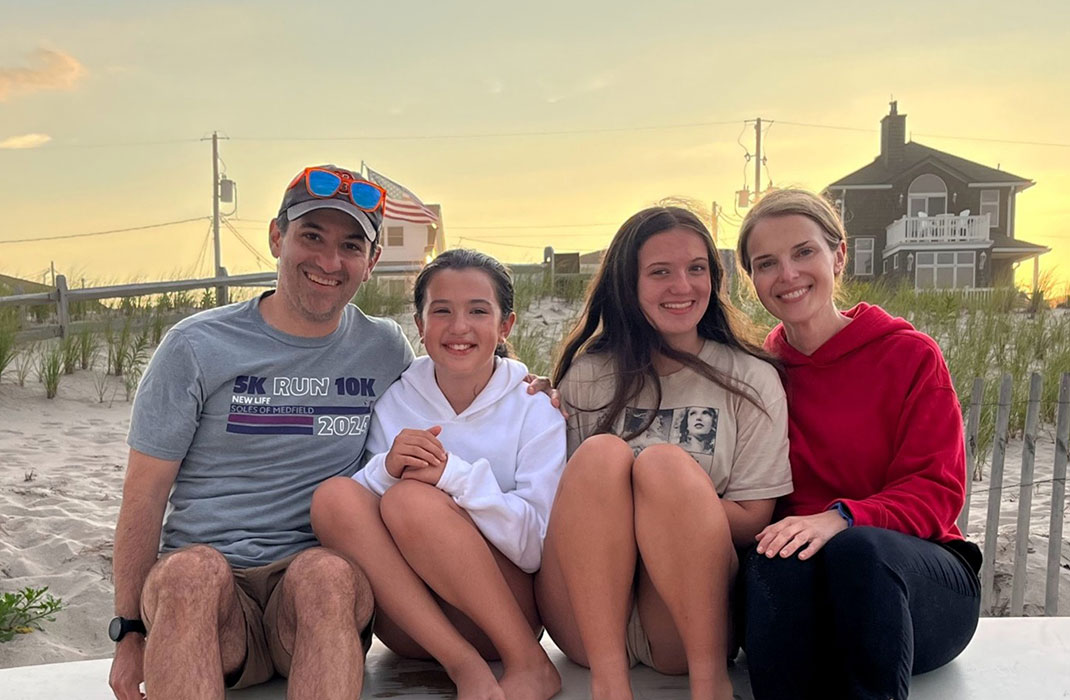 Group photo of family of four at the beach, smiling and sitting on the sand