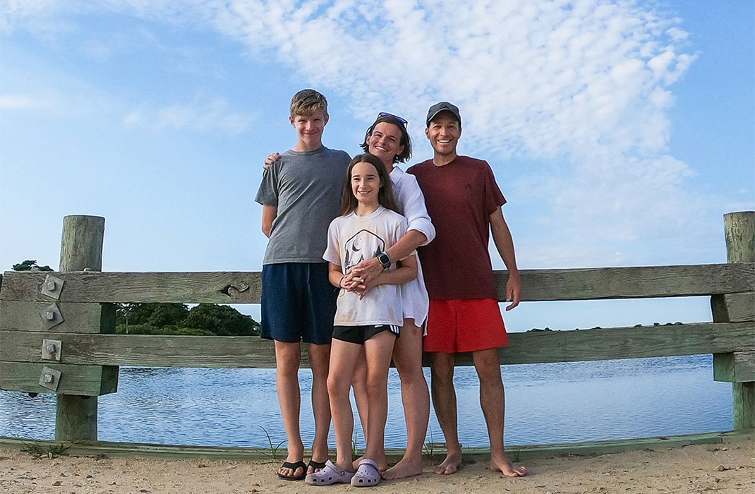 Happy group photo of husband, wife, teenage son and preteen daughter at the beach.