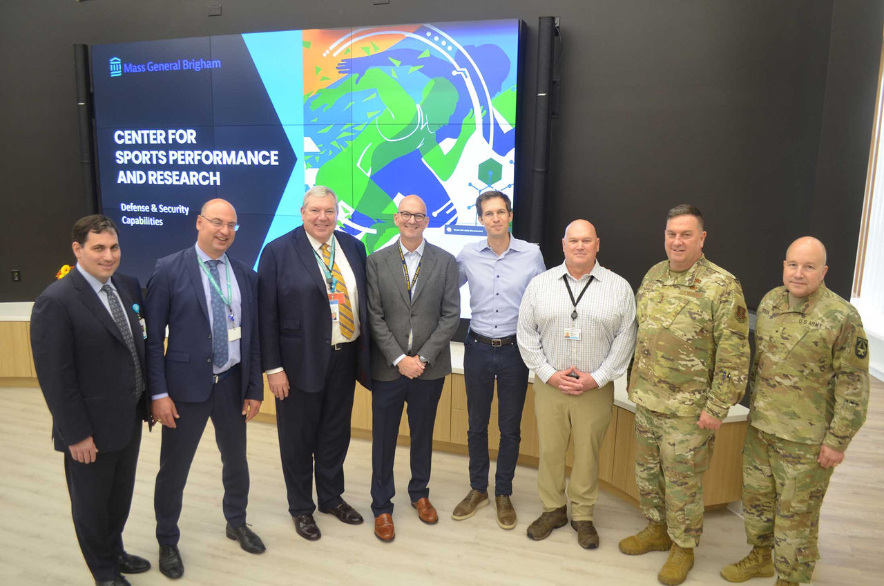 Congressman Jake Auchincloss, CSPAR program director Mark Stephenson, and military and civilian personnel posing in front of a sign for CSPAR.