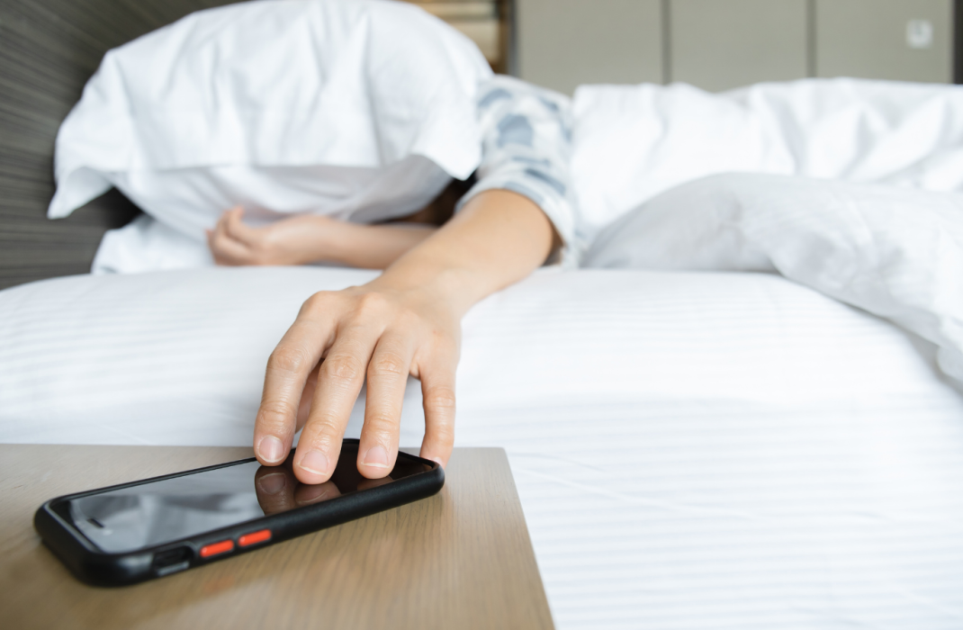 someone sleeping pressing snooze on their phone alarm clock
