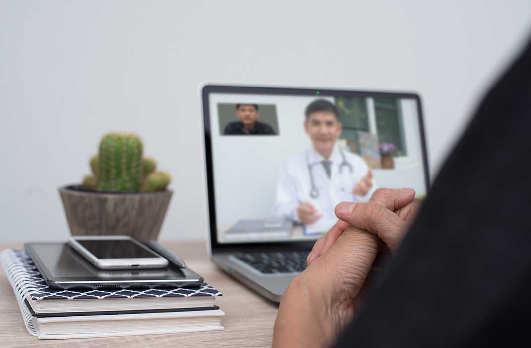 An open laptop displaying a virtual care session with a white-coated doctor.