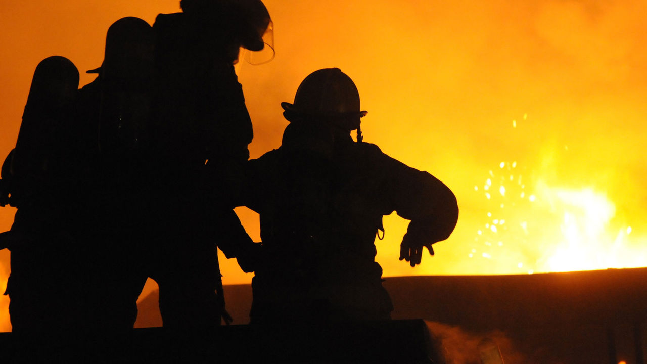 Silhouette of three firefighters fighting a fire.