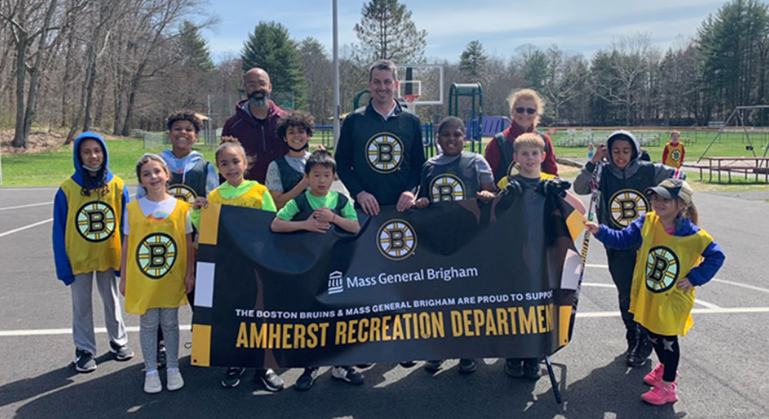 group photo with young participants and coach from the Boston Bruins youth street hockey clinic with an Amherst recreation department banner
