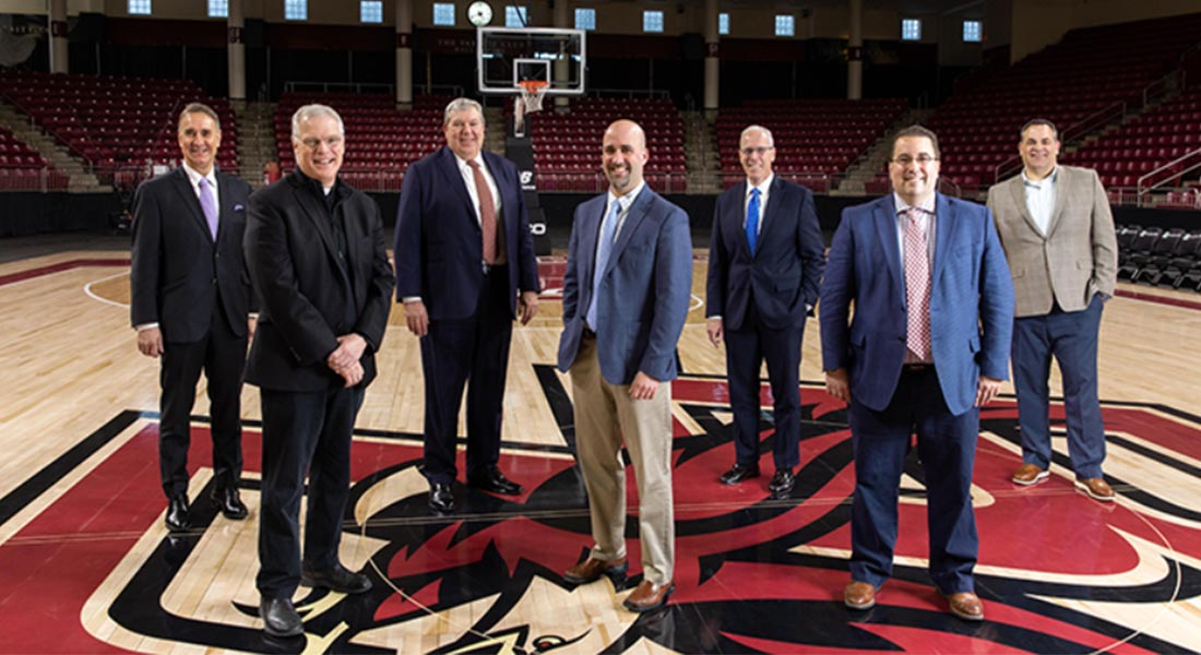 7 individuals smiling and standing in an indoor basketball court