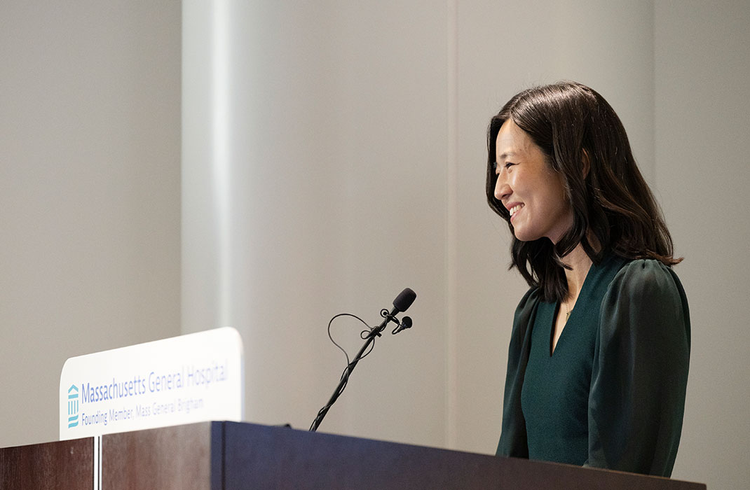 Mayor Michelle Wu smiling while speaking at a podium featuring a Massachusetts General Hospital logo on it