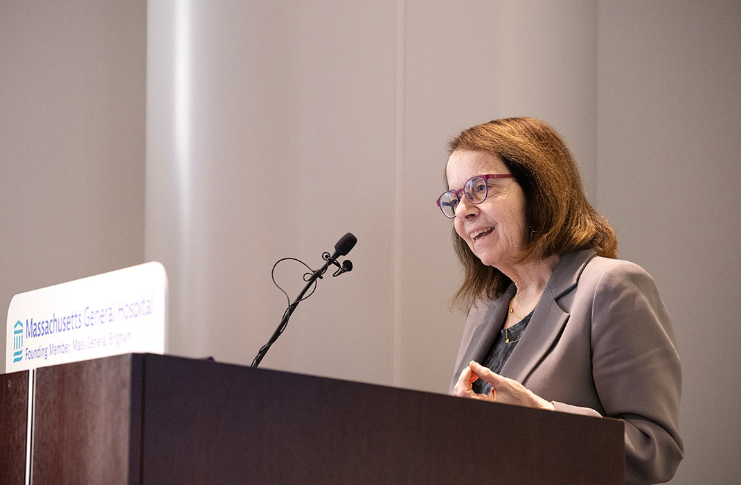 Dr. Anne Klibanski smiling while speaking at a podium featuring a Massachusetts General Hospital logo on it