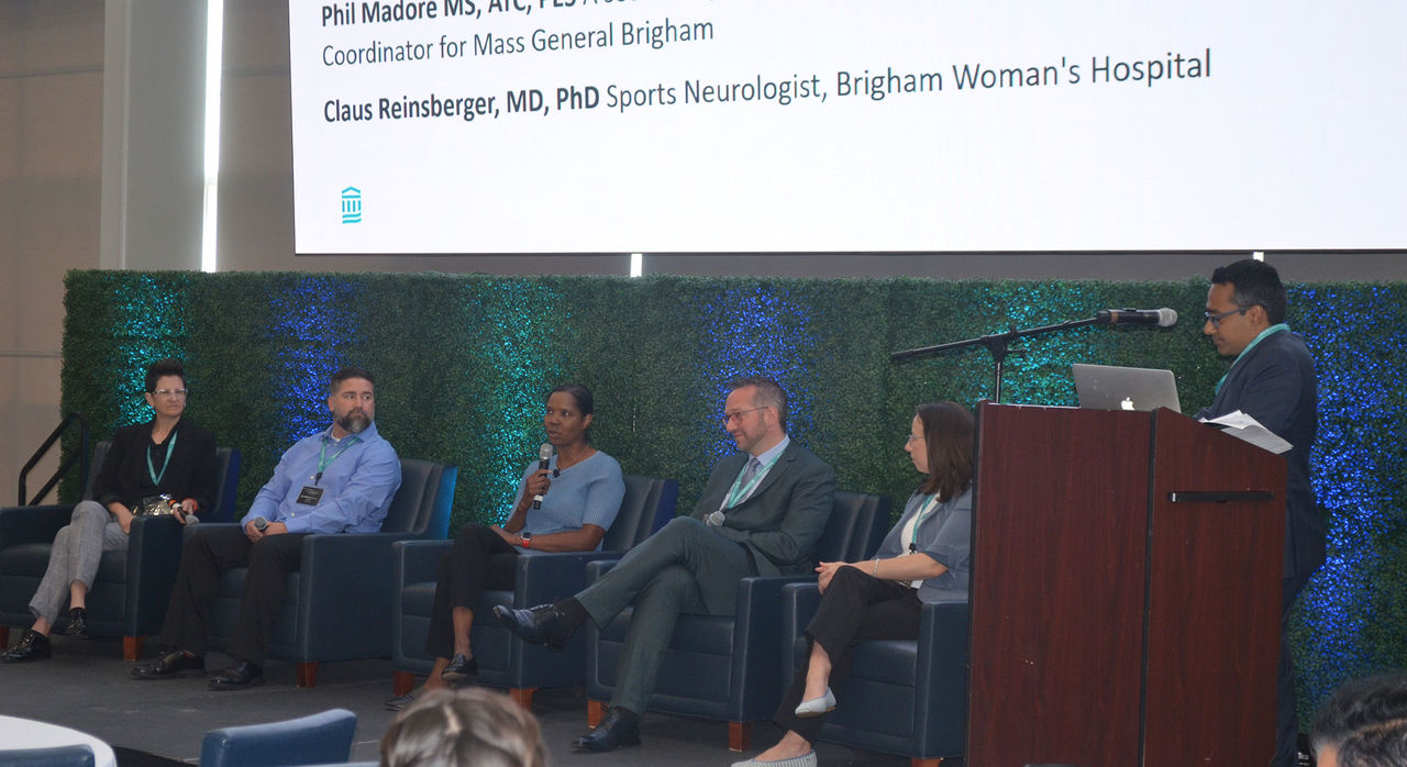 5 panel members sitting on stage with a moderator by the podium