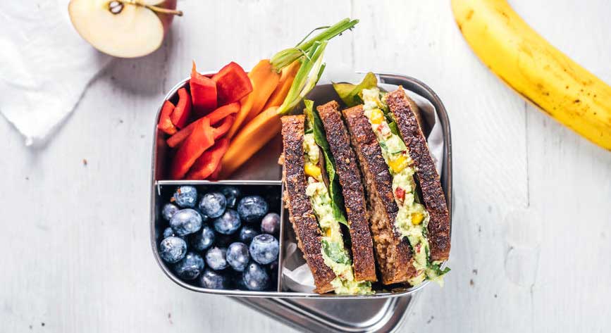 A lunchbox with a sandwich, vegetables and fruits.