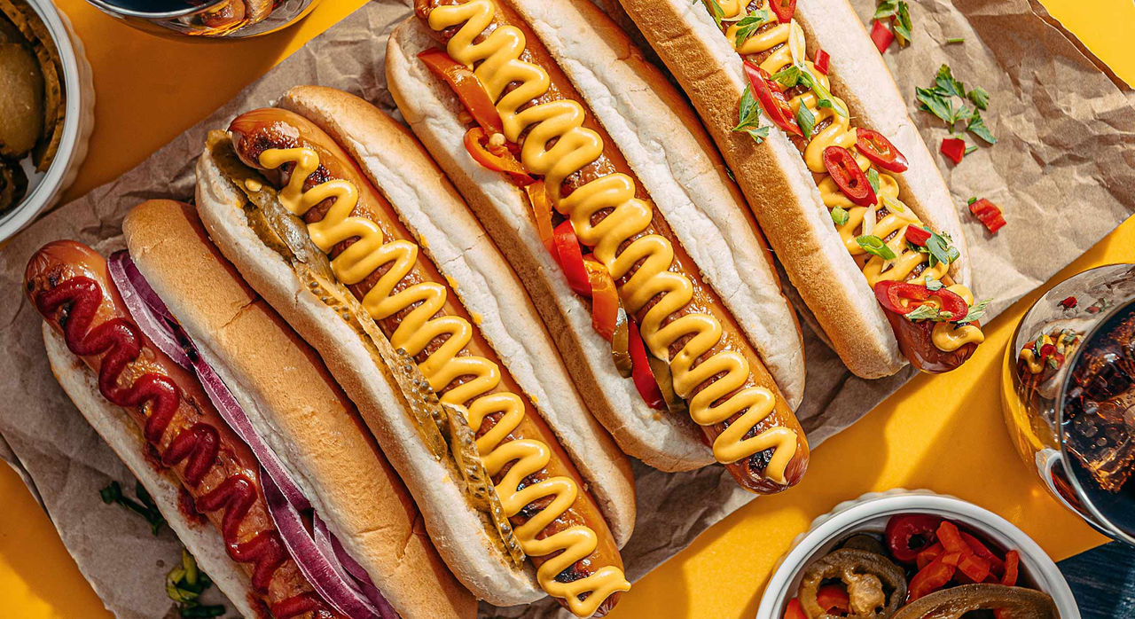 A row of hot dogs with gourmet toppings like pickled onions or red peppers.