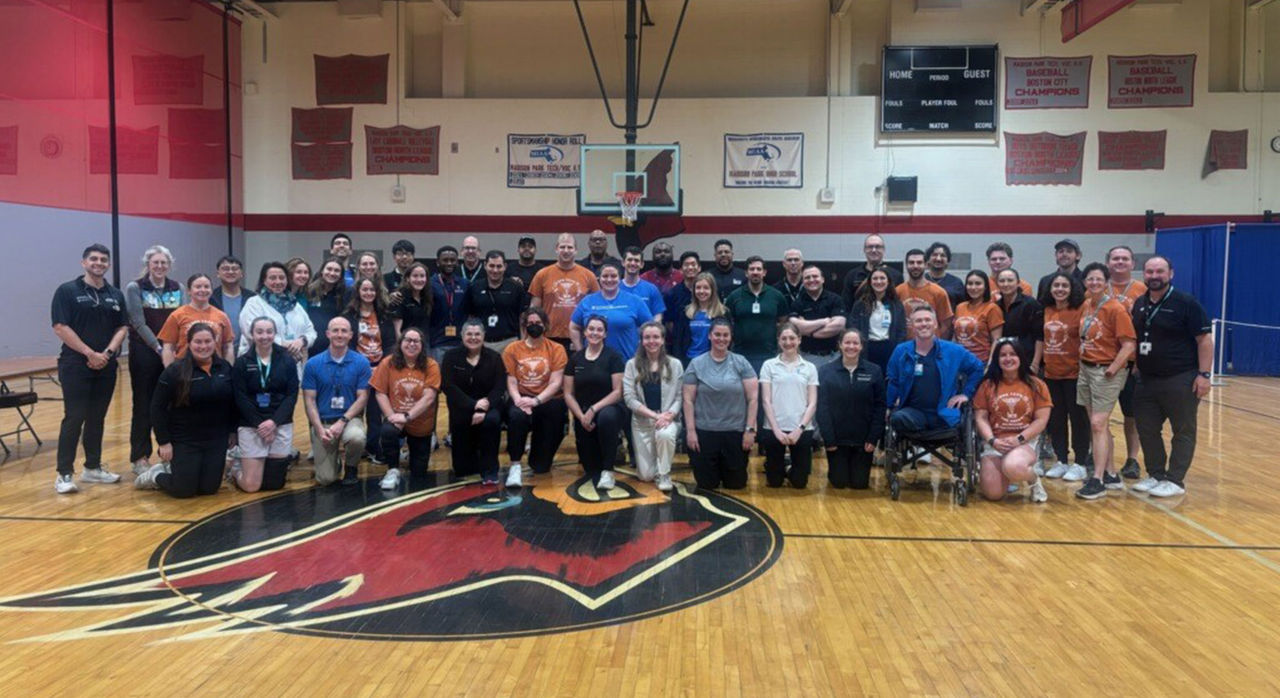 A large group of Mass General Brigham Sports Medicine team members pose in a gymnasium.