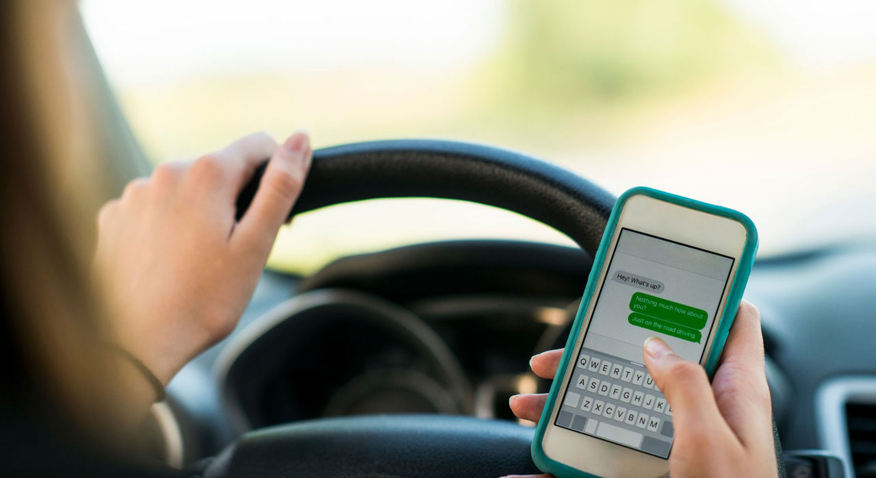 A woman texts with one hand while driving with the other.