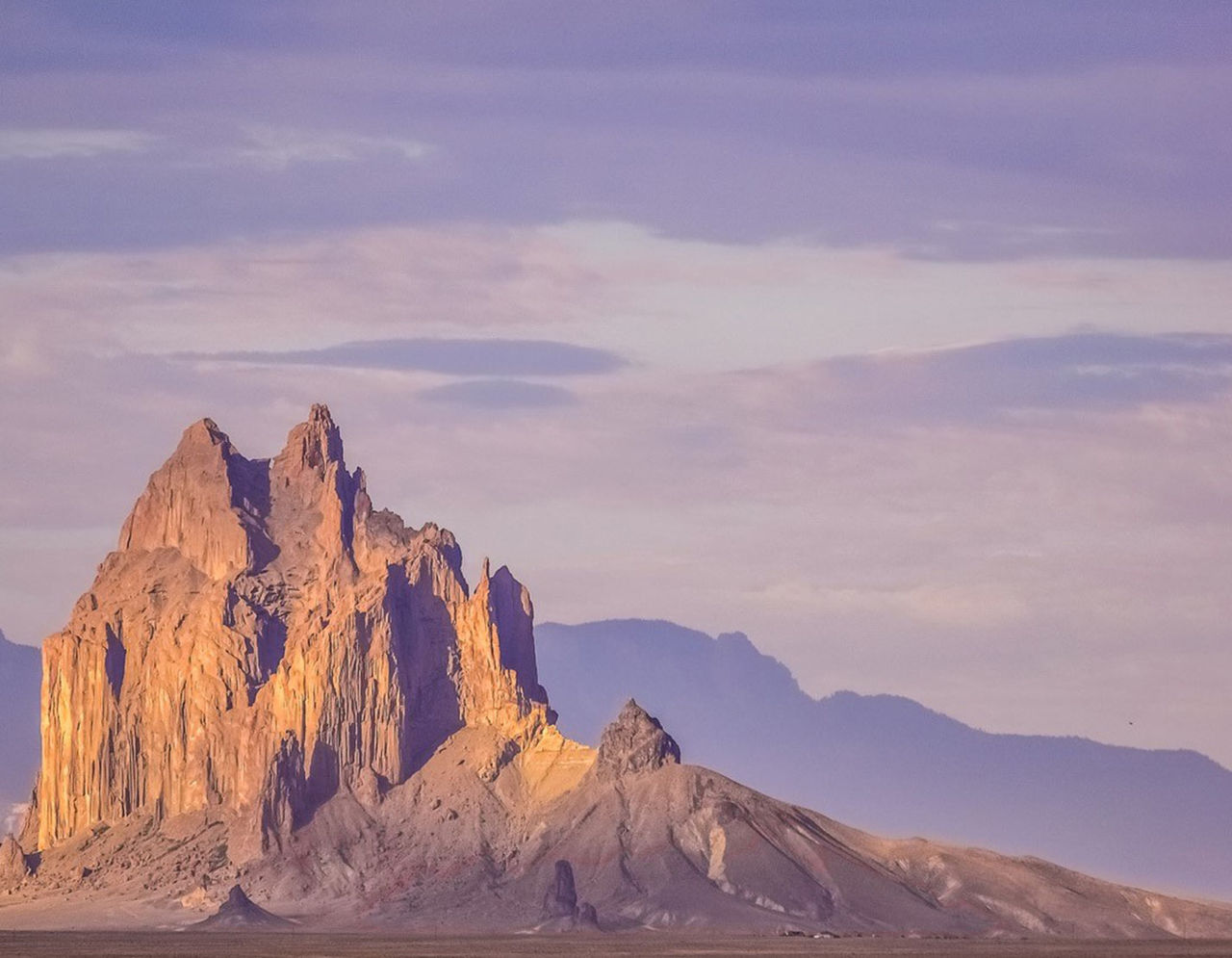 The Shiprock rock formation sitting above the desert at sunrise