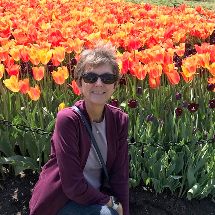 carol goodermote wearing sunglasses and smiling in a field of tulips