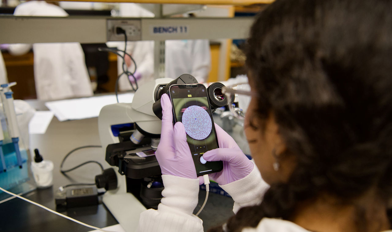 student in laboratory viewing images on cell phone