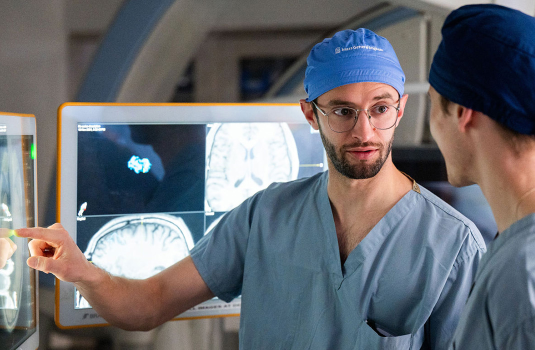 Two neurology clinicians dressed in scrubs reviewing scans on monitors