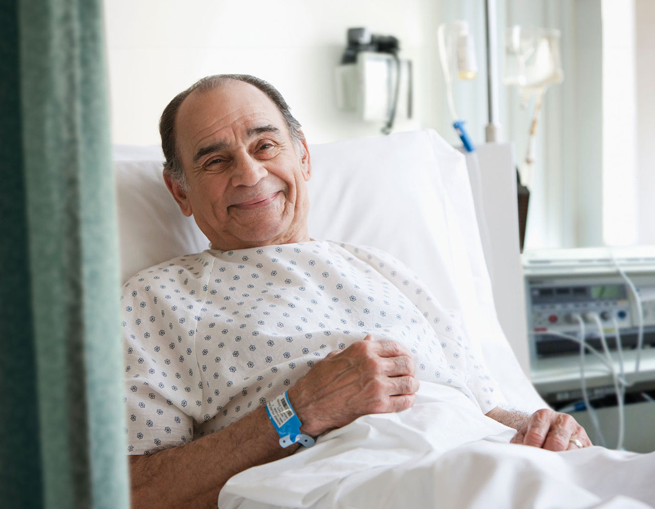 older male patient in hospital room smiling from bed