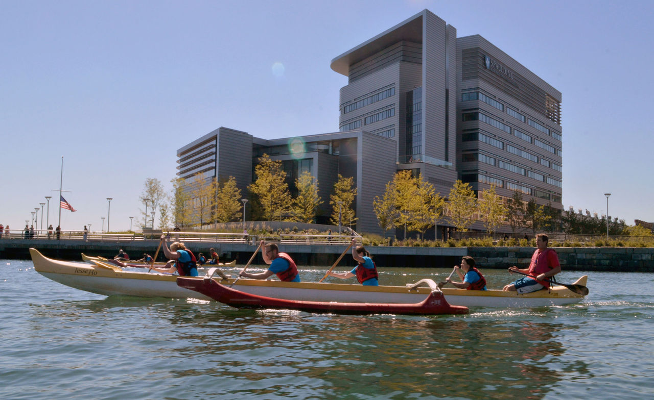 Rowers in water with Spaulding Rehabilitation Hospital in background 