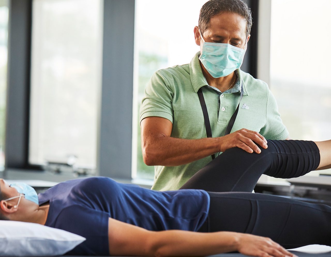 Male provider performing knee exercises on female patient laying on table 