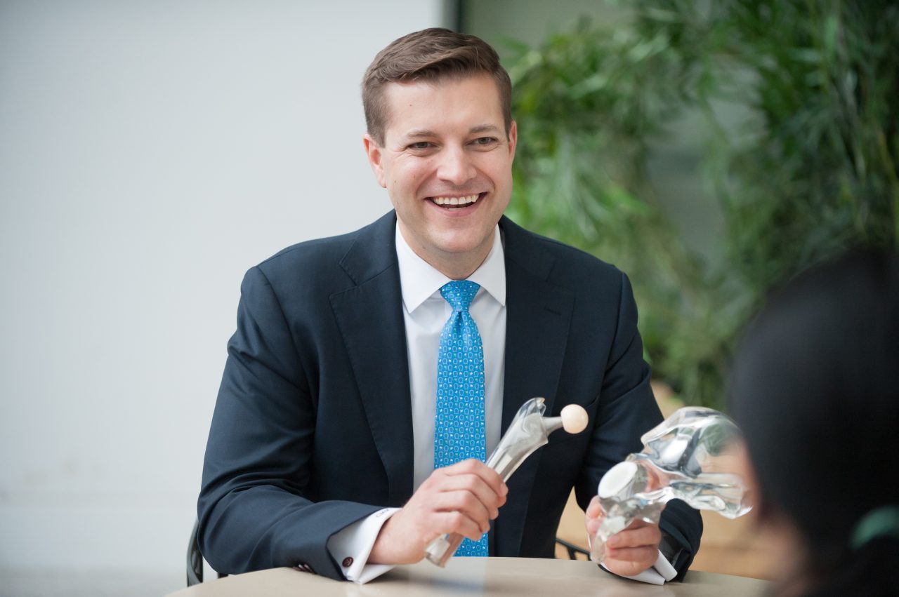 Male provider smiling holding a model of a hip joint