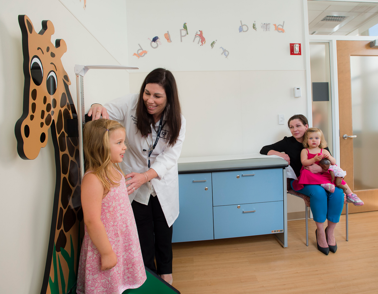 Doctor measuring height of child at Child Development Center with mother and child in chair