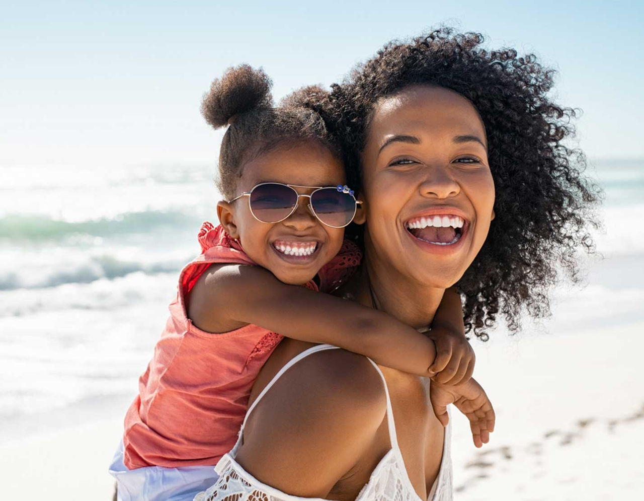 mother with young daughter on her back smiling at the beach