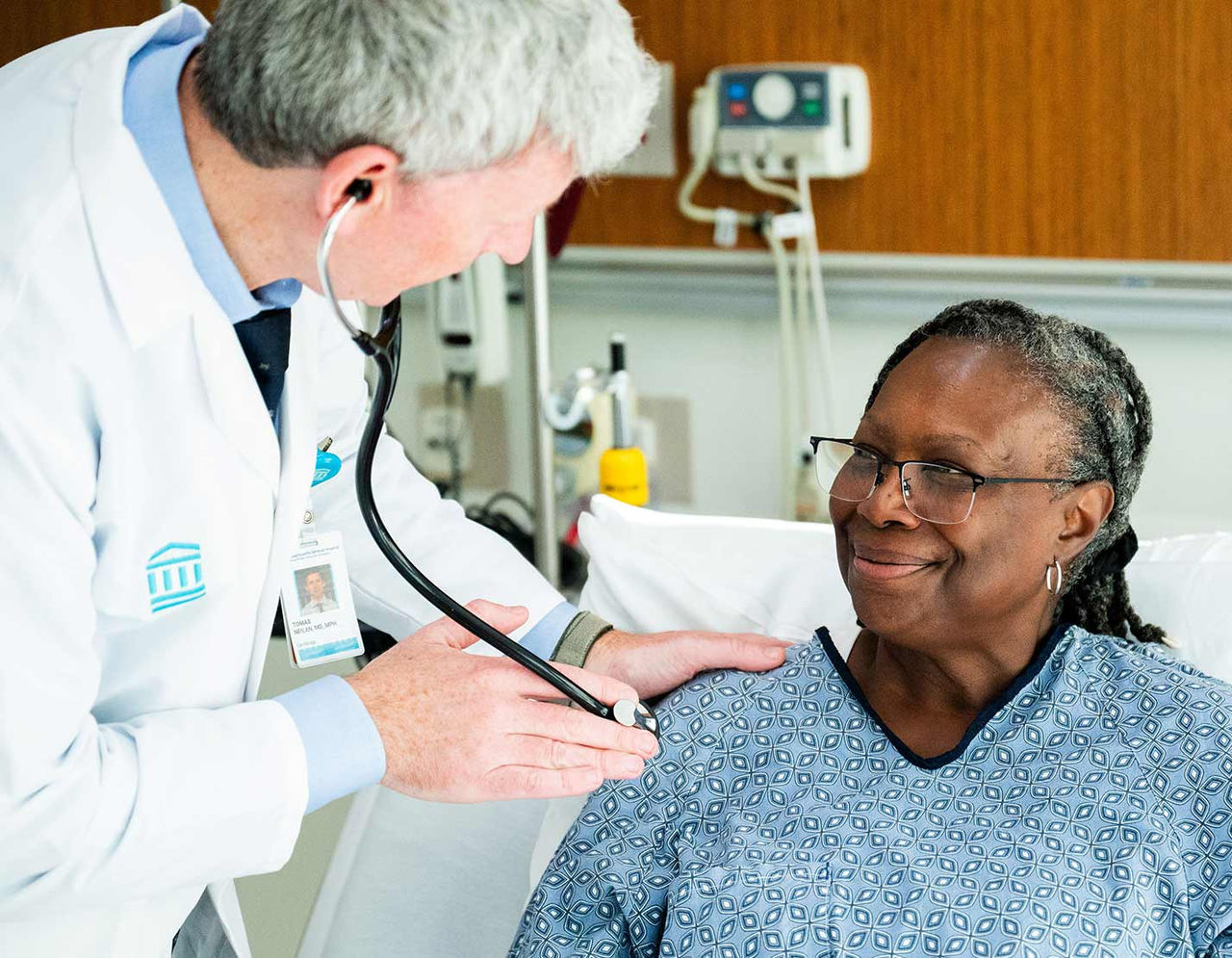 male provider with female patient at bedside using stethoscope