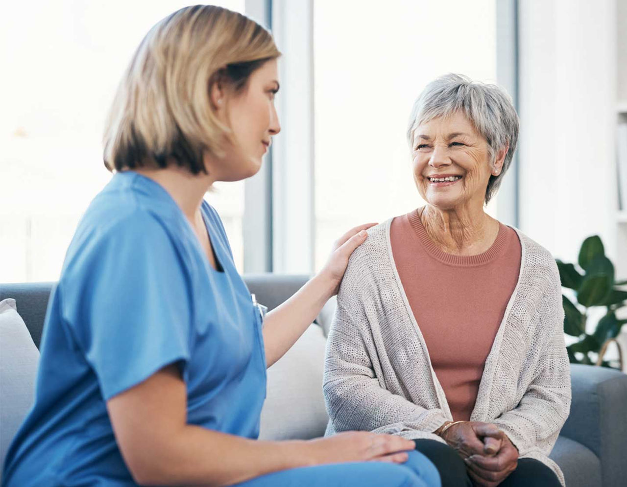 female provider with hand on shoulder of smiling older female patient