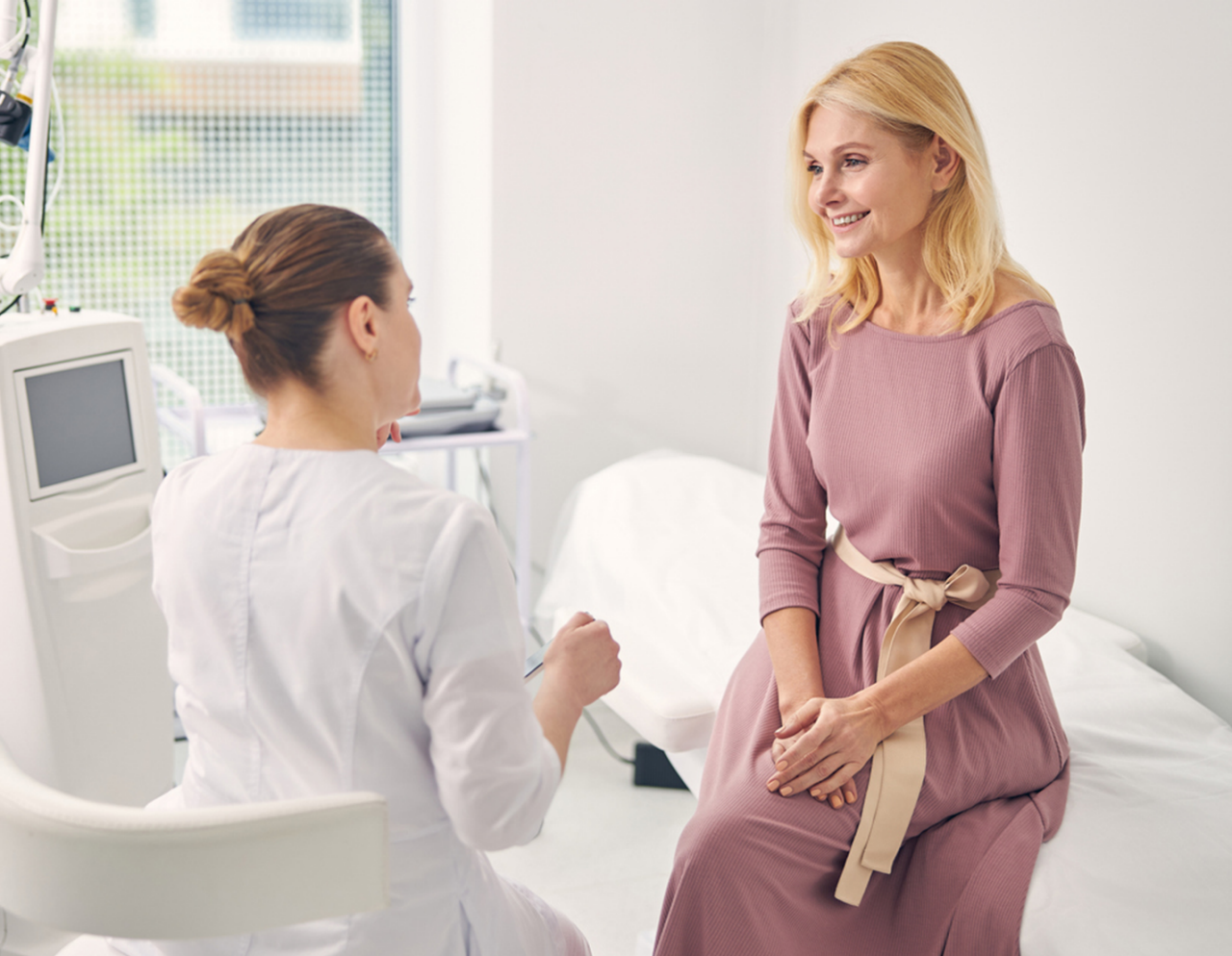 A patient sits on an exam table while speaking with a healthcare professional. 
