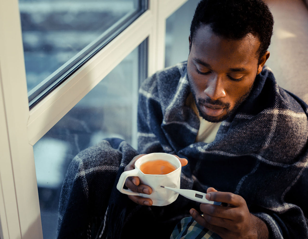 Man with blanket, cup of tea, and thermometer
