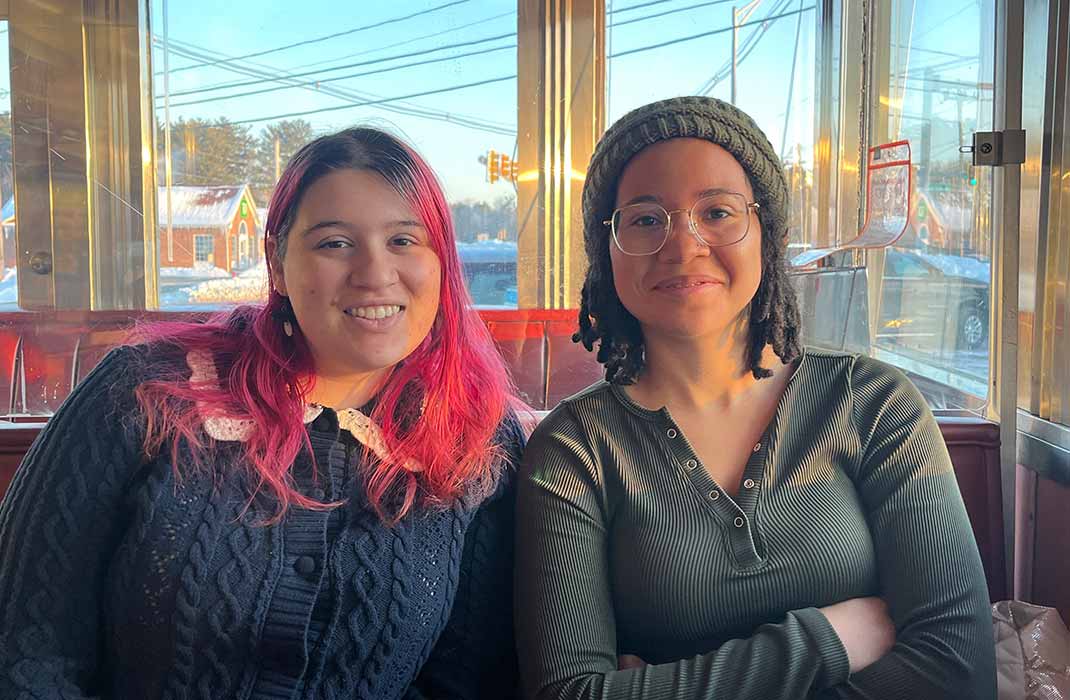 Two people sitting together in sunlit diner booth.