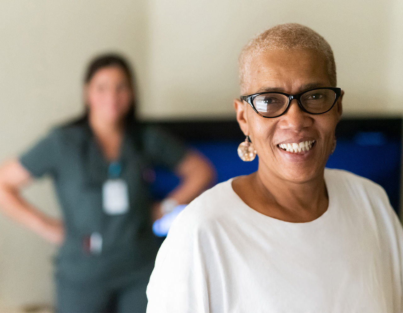 Patient smiles at the camera while a provider in scrubs stands in the background