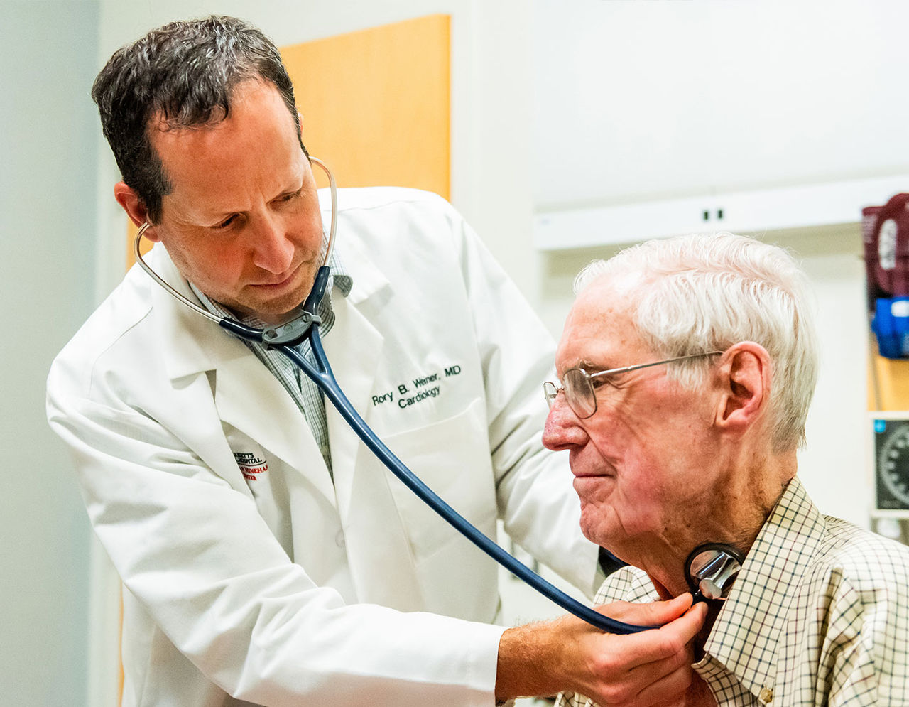 male provider using stethescope on neck of older male patient in exam room