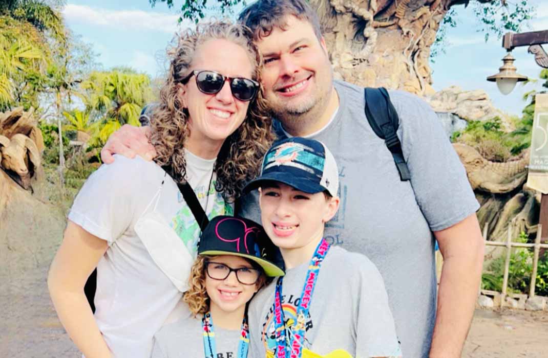 A mother and father smiling and hugging two of their kids who are wearing caps and smiling