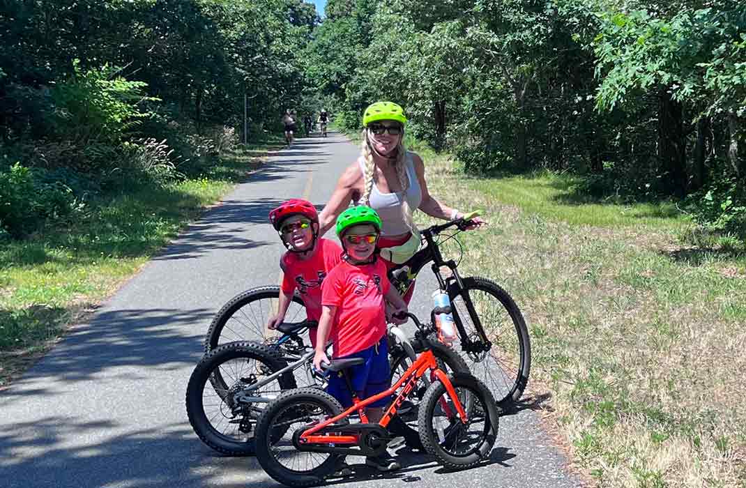 Tara and her two sons go for a bike ride on a sunny day in a park with trees lining the pathway