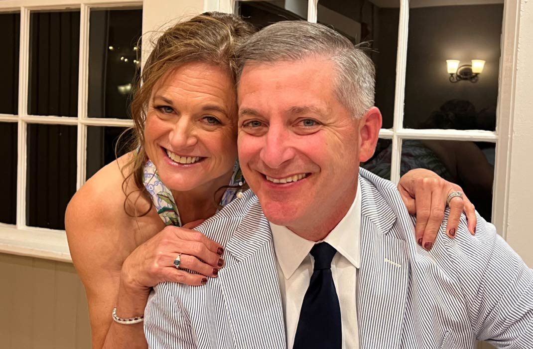 A man and woman are dressed in formal attire, smiling and posing together in an indoor setting.