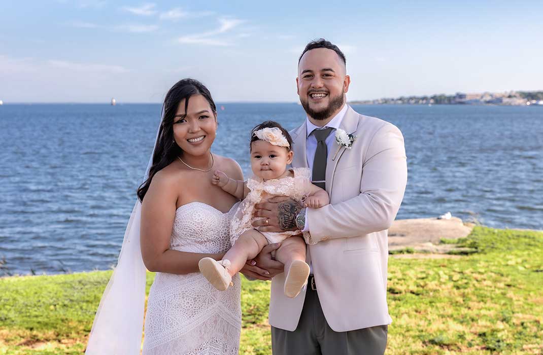 Katherine and her new husband Shawn in their wedding clothes, holding their baby, Amari, between them.