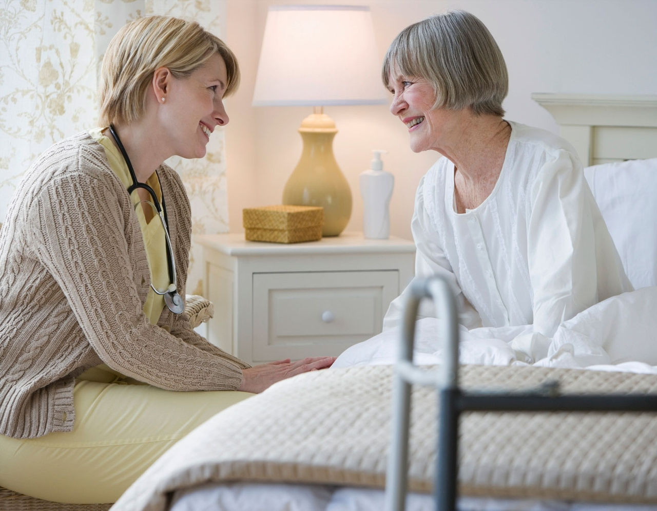 Home care provider and elderly patient holding hands at bedside 