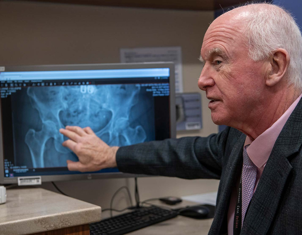 Doctor examines hip X-ray on computer monitor.