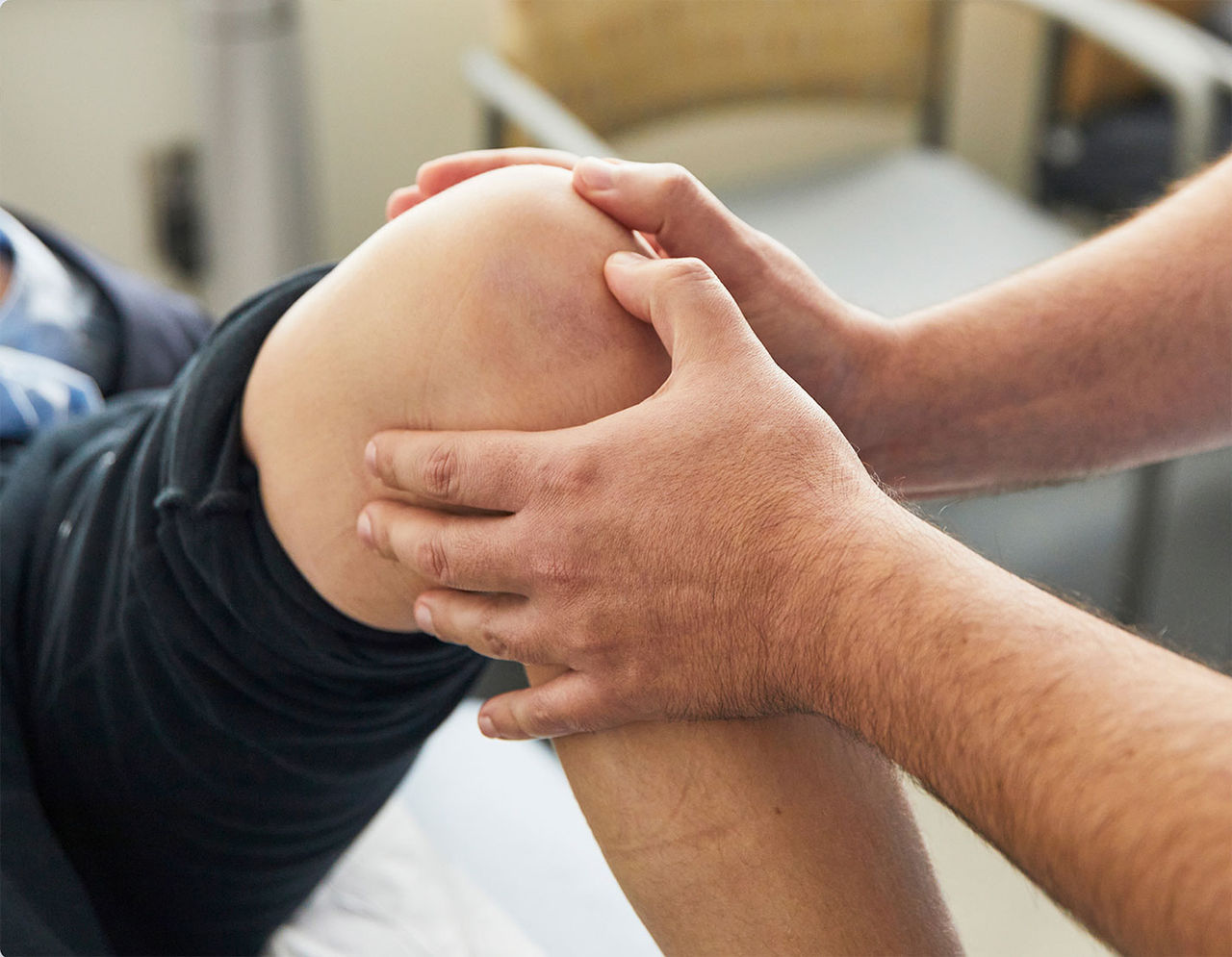 A close-up of a physical therapist's hands examining a patient's knee during a therapy session