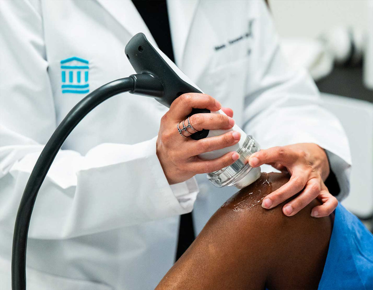 A healthcare professional uses a medical therapy device on a patient's knee in a clinical setting